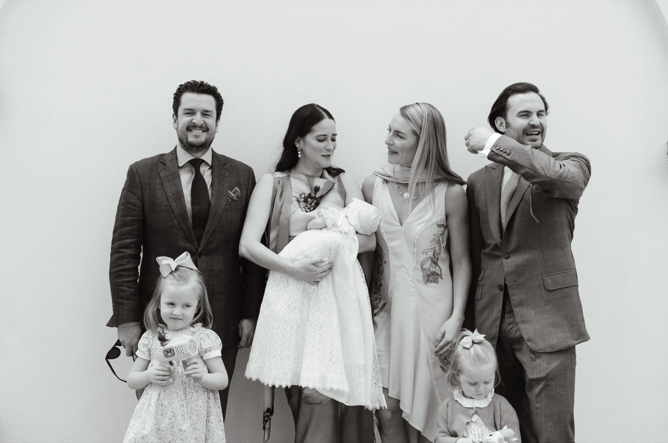 Familia elegante posando junto a un bebé con faldón de bautizo de encaje, en blanco y negro