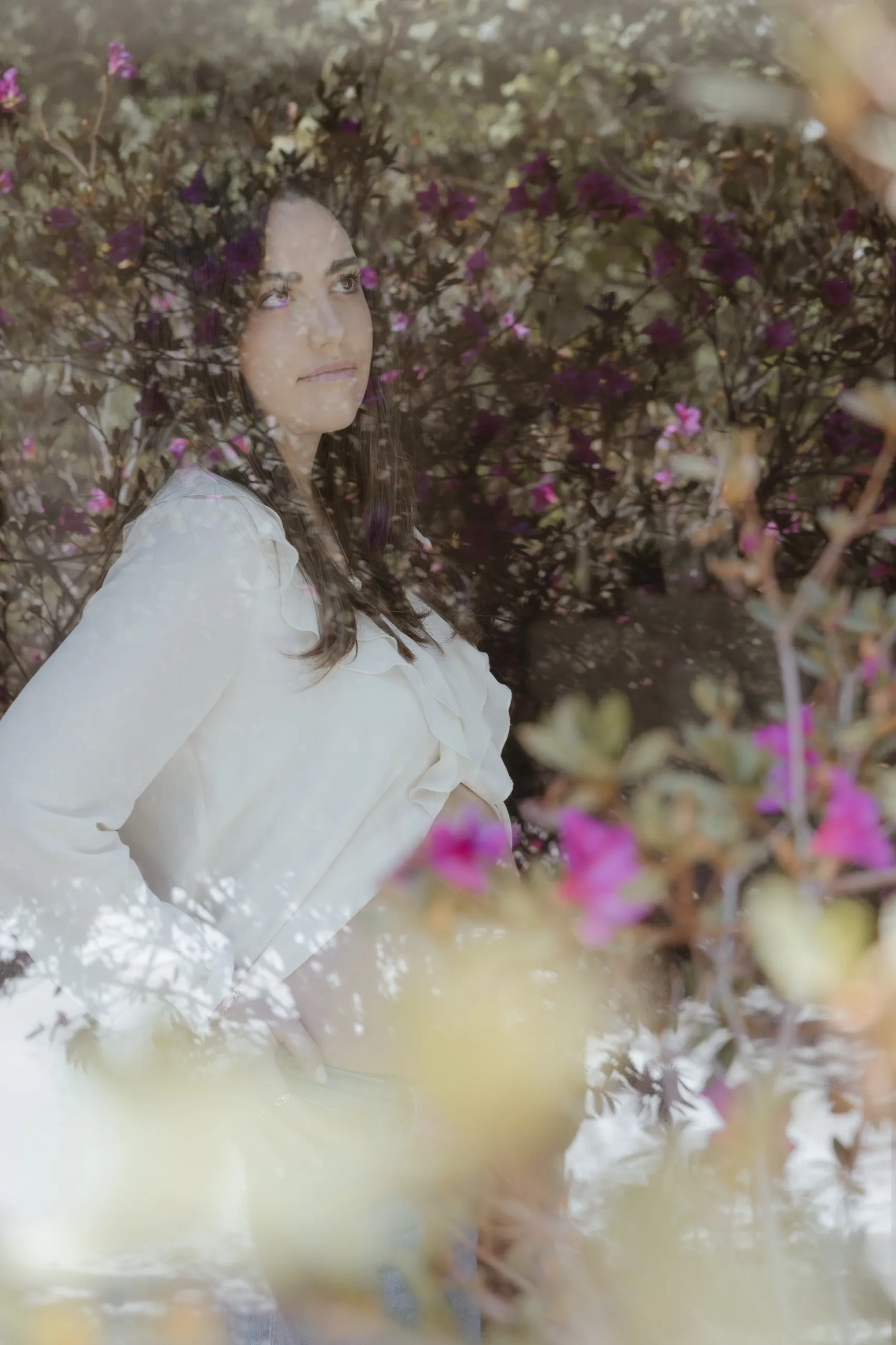Mujer joven con blusa blanca entre flores rosas en un jardín, con efecto soñador