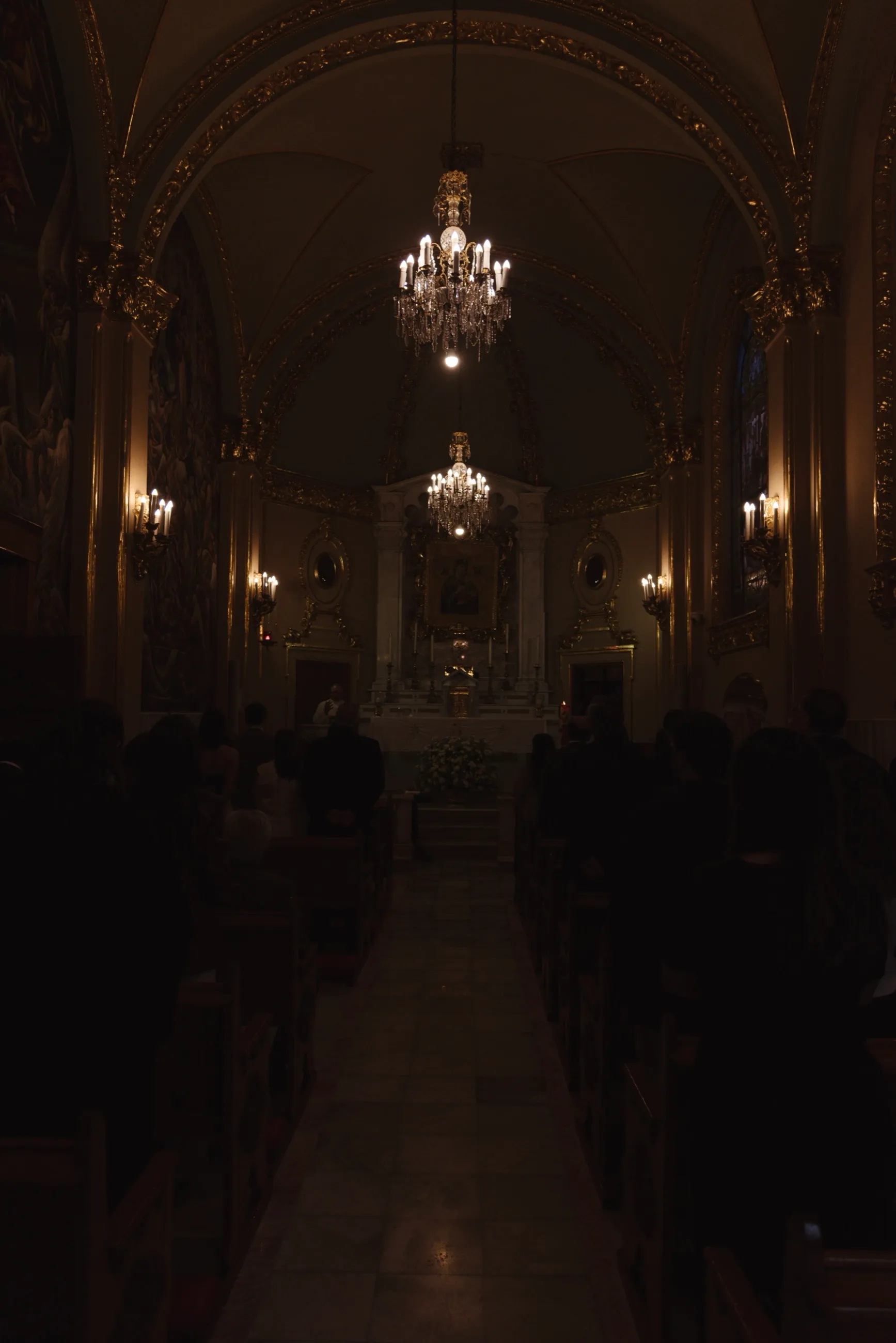 Interior en penumbra de una iglesia barroca durante una ceremonia de boda, con candelabros iluminando el altar