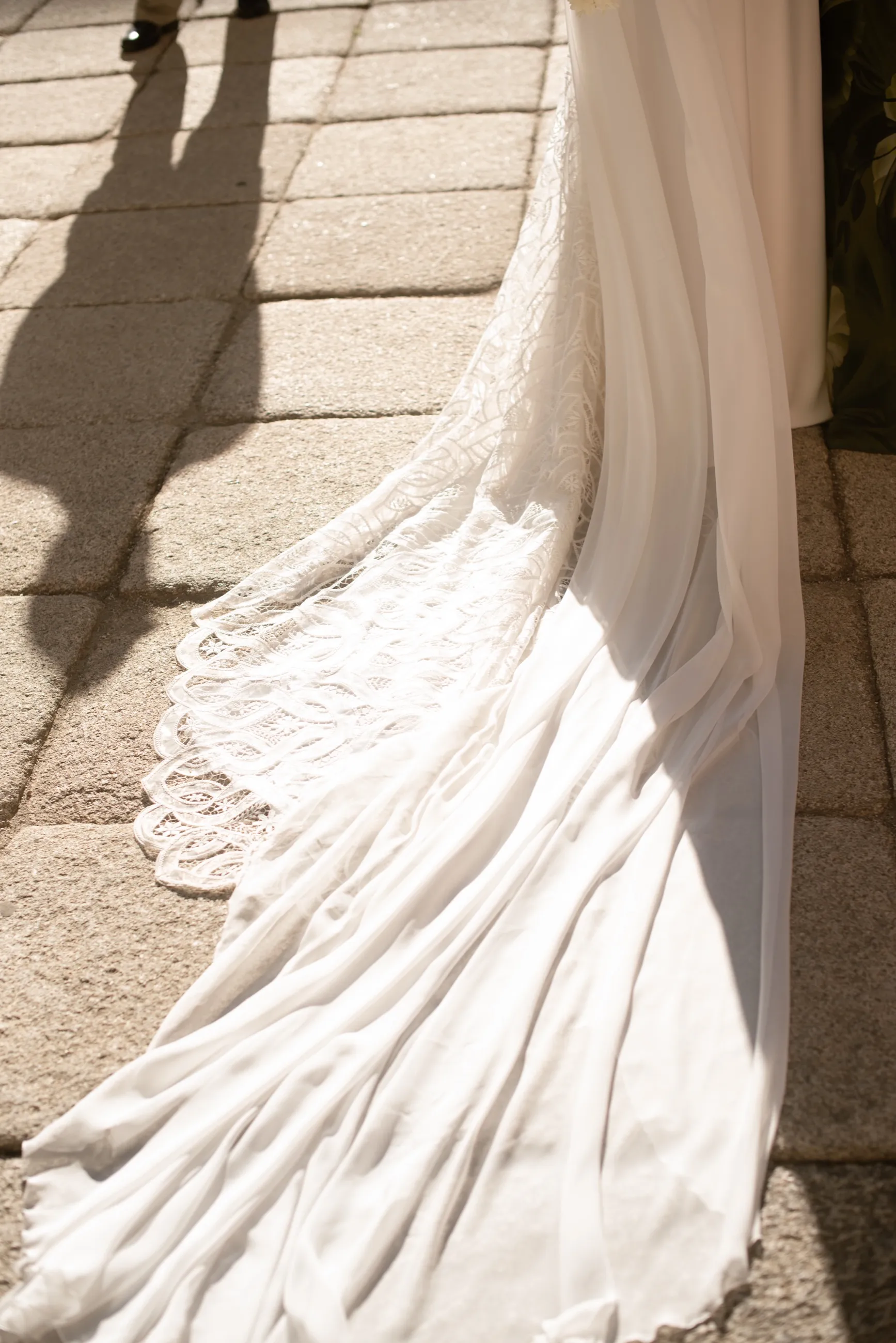 Cola de vestido de novia con encaje extendida sobre suelo de piedra bajo el sol